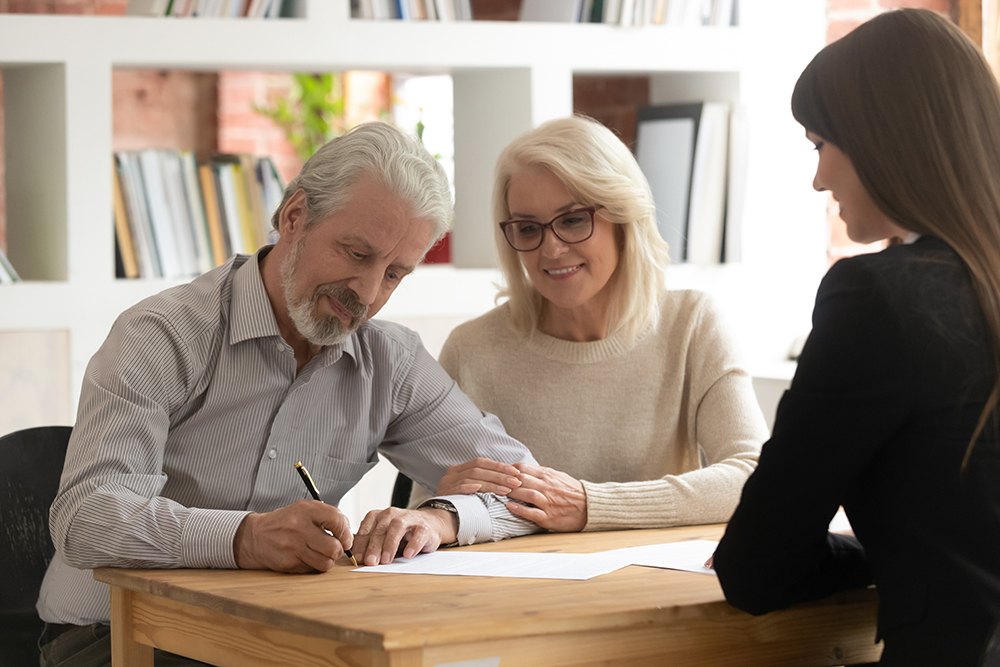 Happy mature clients sign contract closing deal with banker
