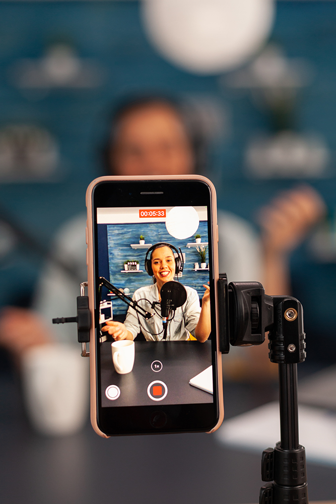 Close up of influencer vlogger record video live broadcast looking at smartphone on tripod at home studio podcast