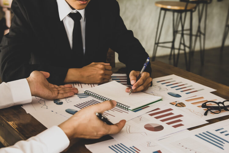 two businessman people holding pen writing a report data, Teamwork discussing meeting point to discuss the graph up and down financial of marketing economy on desk. venture